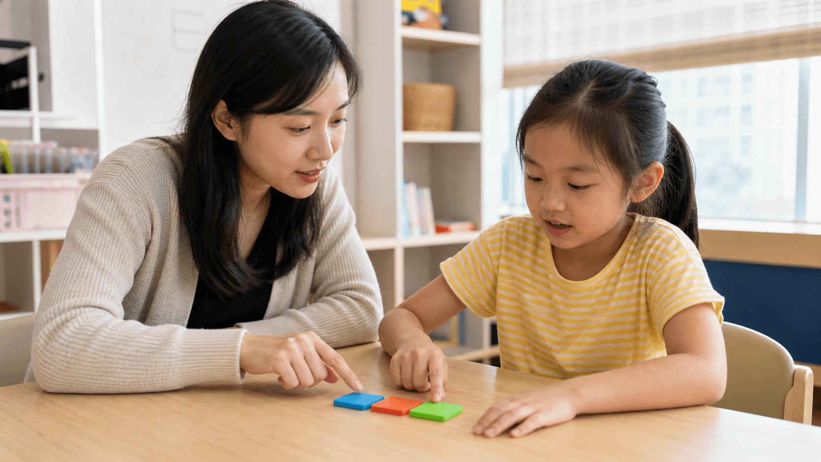 Tutor guiding a primary pupil to blend sounds from left to right with coloured phonics tiles